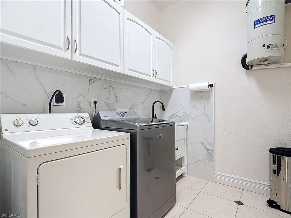 Washroom featuring cabinet space, washing machine and clothes dryer, and light tile patterned floors