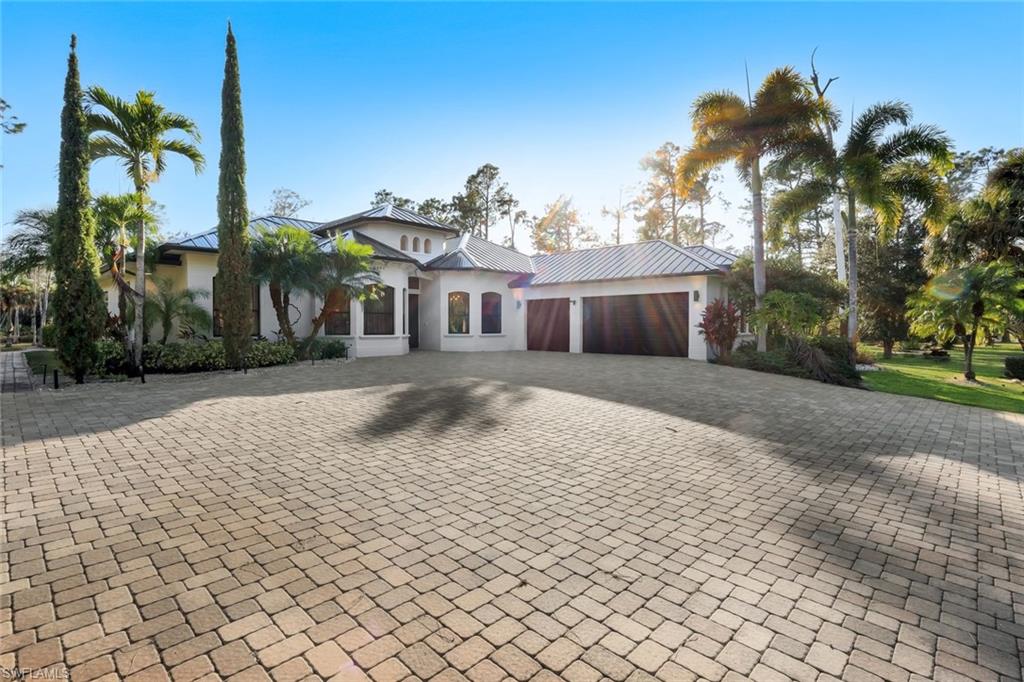 View of front of property featuring stucco siding, a garage, driveway, and a metal roof