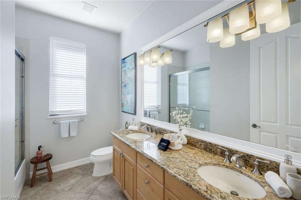 Full bathroom with double vanity, combined bath / shower with glass door, light tile patterned floors, and hanging lights