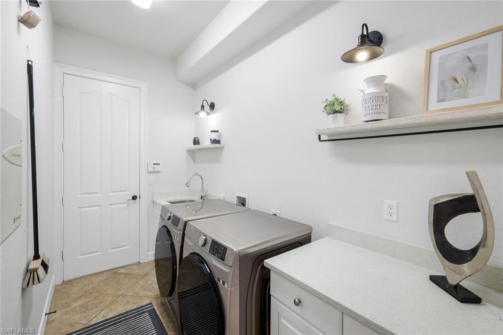 Laundry area with washing machine and clothes dryer, light tile patterned floors, and cabinet space
