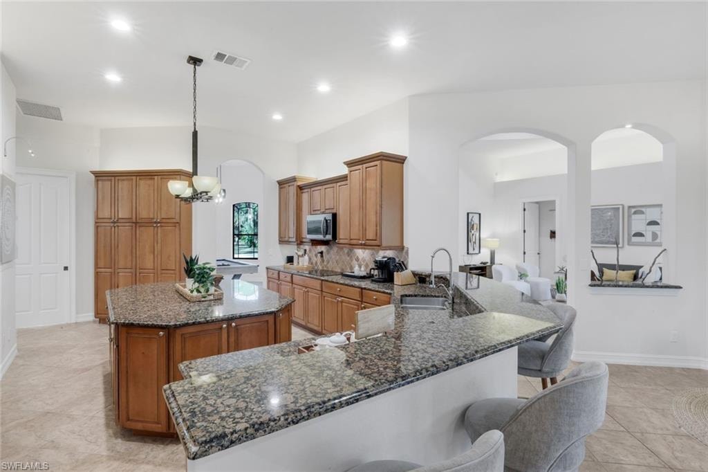 Kitchen featuring arched walkways, wood finish cabinetry, dark stone countertops, a peninsula, and a center island