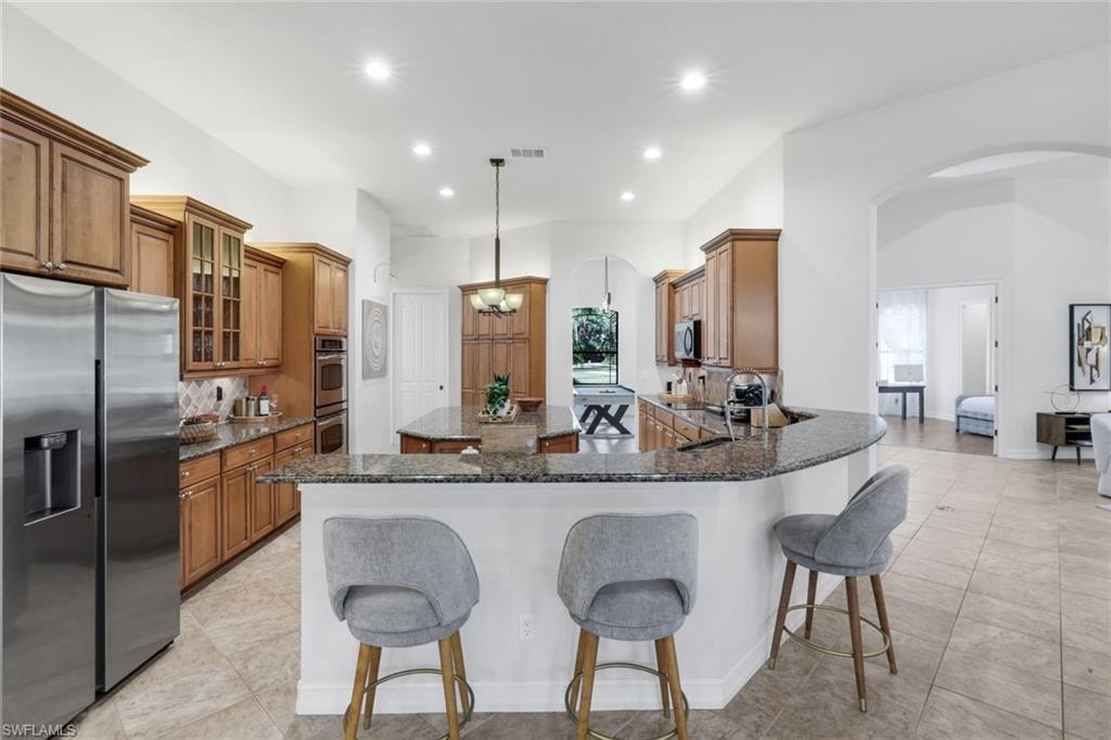 Kitchen featuring wood finish cabinetry, dark stone counters, stainless steel appliances, and a breakfast bar