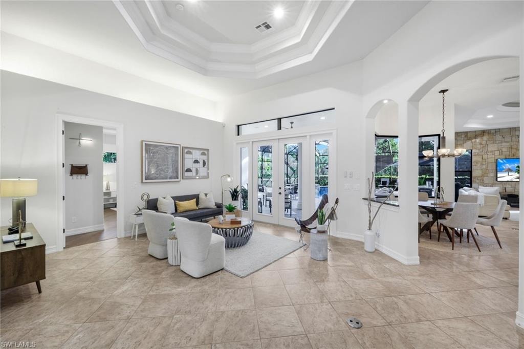 Living room with a raised ceiling, suspended lighting, arched walkways, and french doors