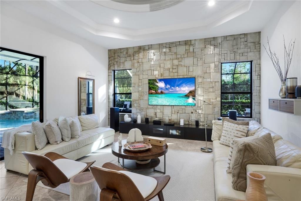 Living area featuring healthy amount of natural light, an accent wall, a raised ceiling, and recessed lighting