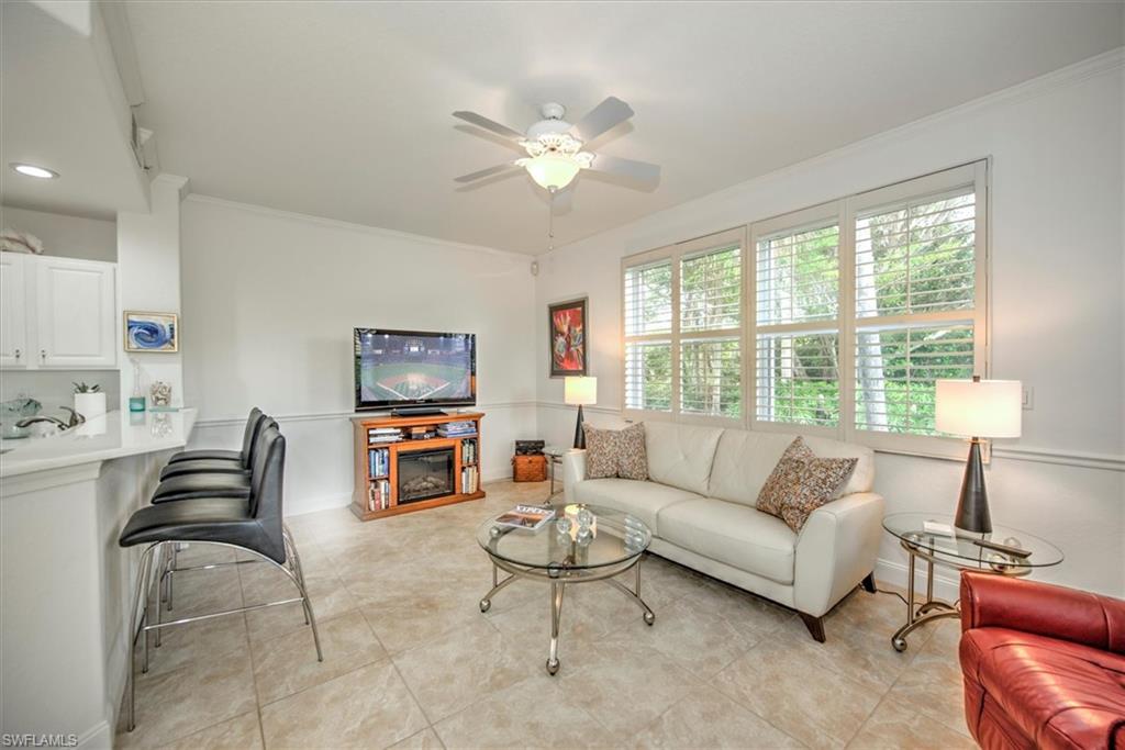Living area with ornamental molding, ceiling fan, a glass covered fireplace, and light tile patterned floors