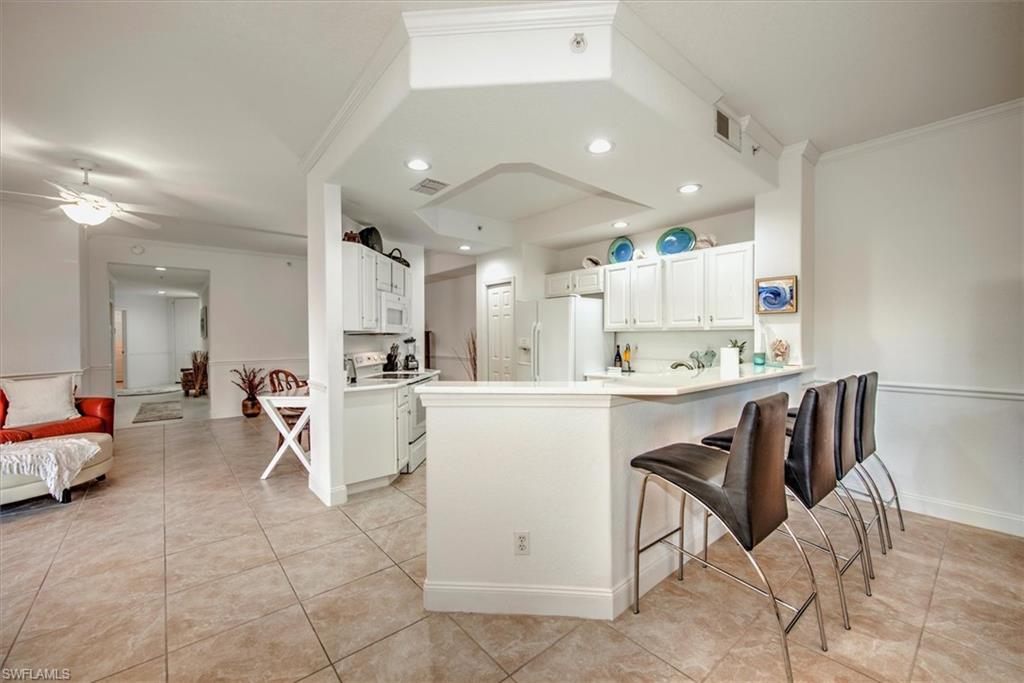 Kitchen featuring white cabinets, light countertops, white appliances, a peninsula, and light tile patterned floors