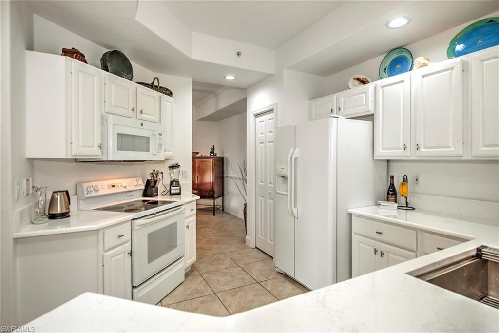 Kitchen with white appliances, white cabinetry, light tile patterned flooring, recessed lighting, and light stone counters