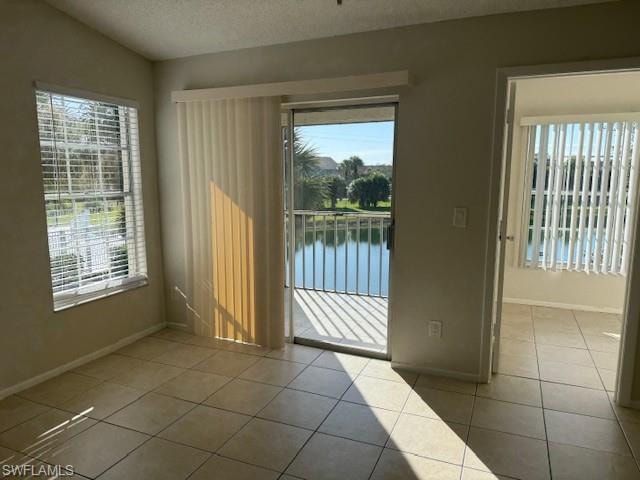 Unfurnished room featuring a water view, a textured ceiling, and light tile patterned floors