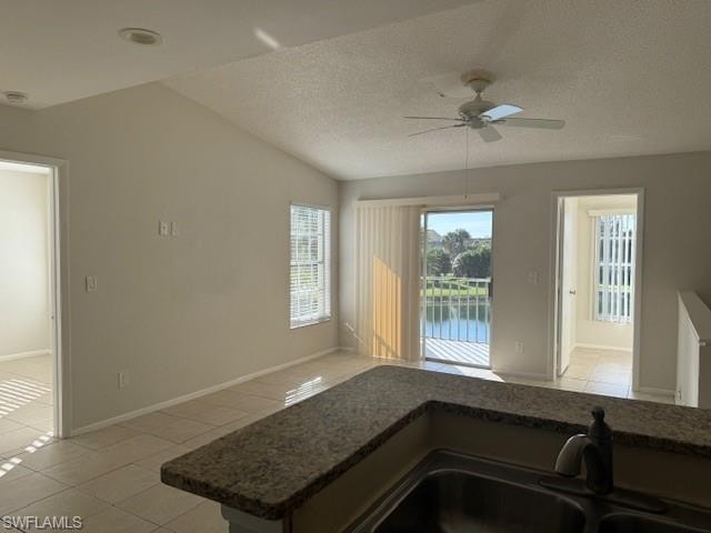 Kitchen featuring light tile patterned flooring, a textured ceiling, a water view, ceiling fan, and lofted ceiling