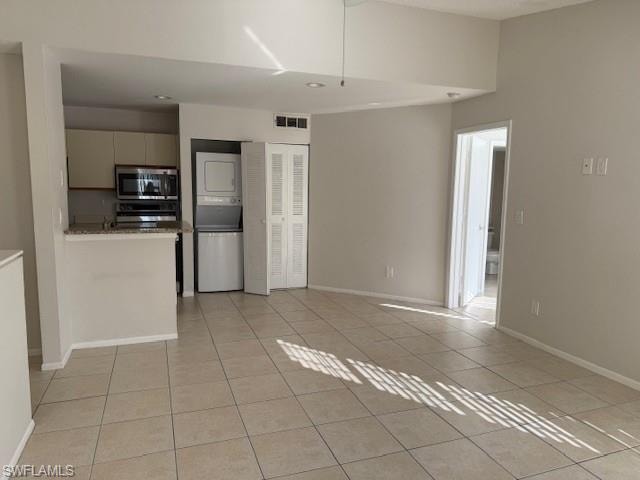 Kitchen featuring estacked washer and dryer, light tile patterned floors, stainless steel microwave, a peninsula, and range