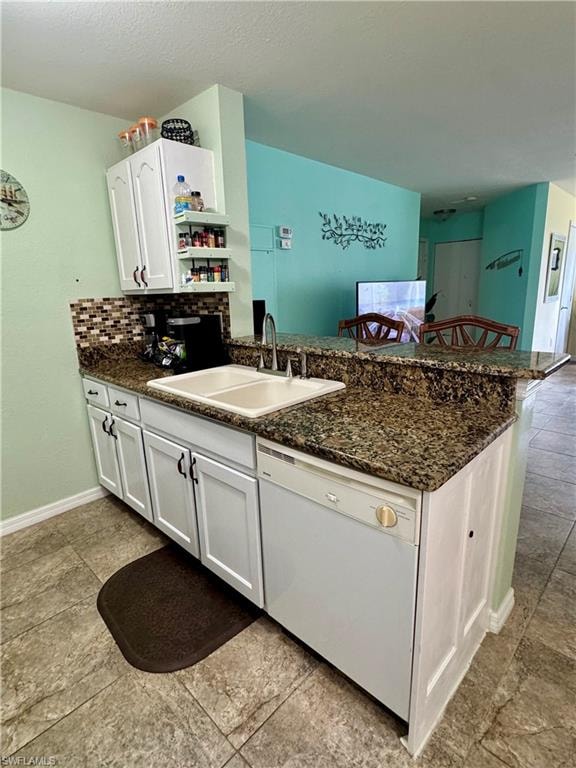 Kitchen with a breakfast bar, white cabinets, dishwasher, a peninsula, and dark stone counters