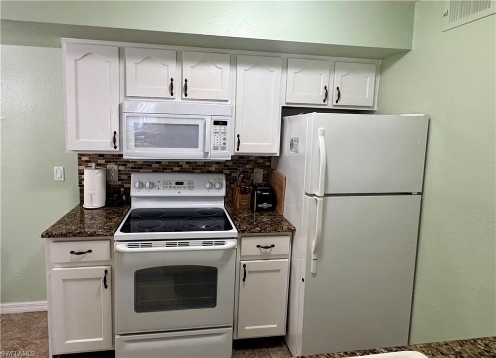 Kitchen featuring white appliances, white cabinets, a textured wall, decorative backsplash, and dark stone countertops