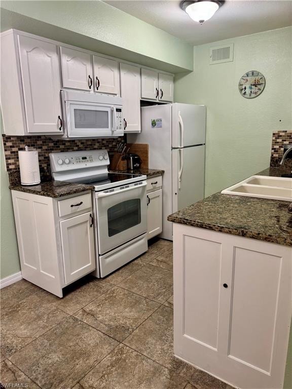 Kitchen featuring white appliances, decorative backsplash, white cabinets, and a textured wall