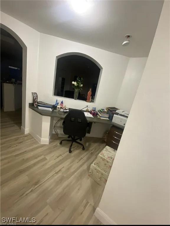 Home office featuring arched walkways, light wood finished floors, and built in study area