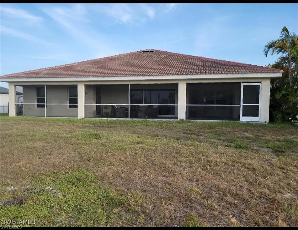 Back of property featuring a yard, a sunroom, and a tiled roof