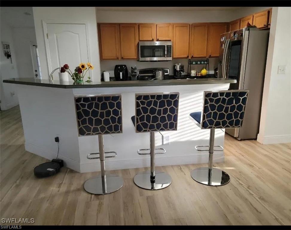 Kitchen featuring dark countertops, stainless steel appliances, a breakfast bar area, and light wood-style floors