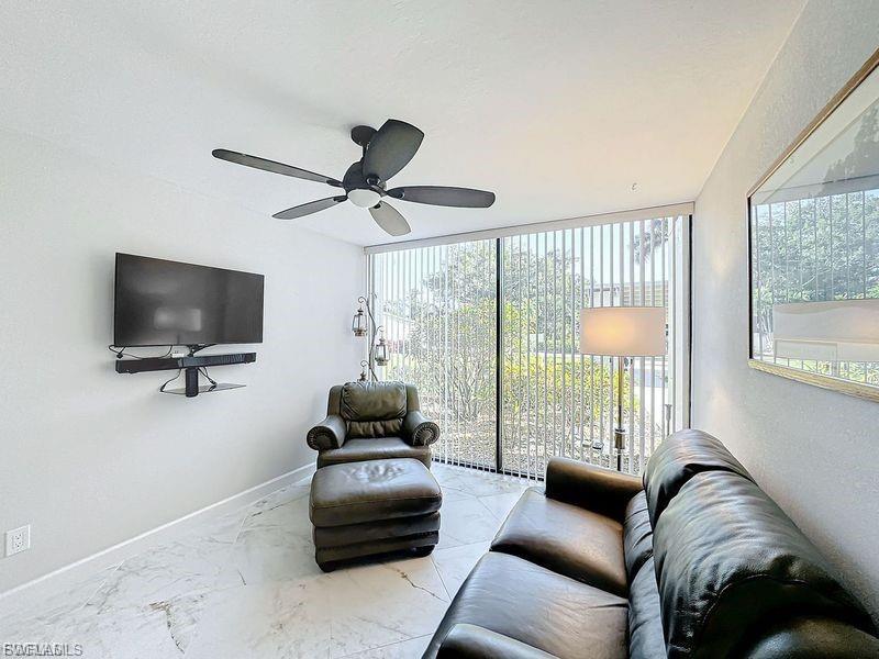 Living area featuring floor to ceiling windows, ceiling fan, and marble finish floors
