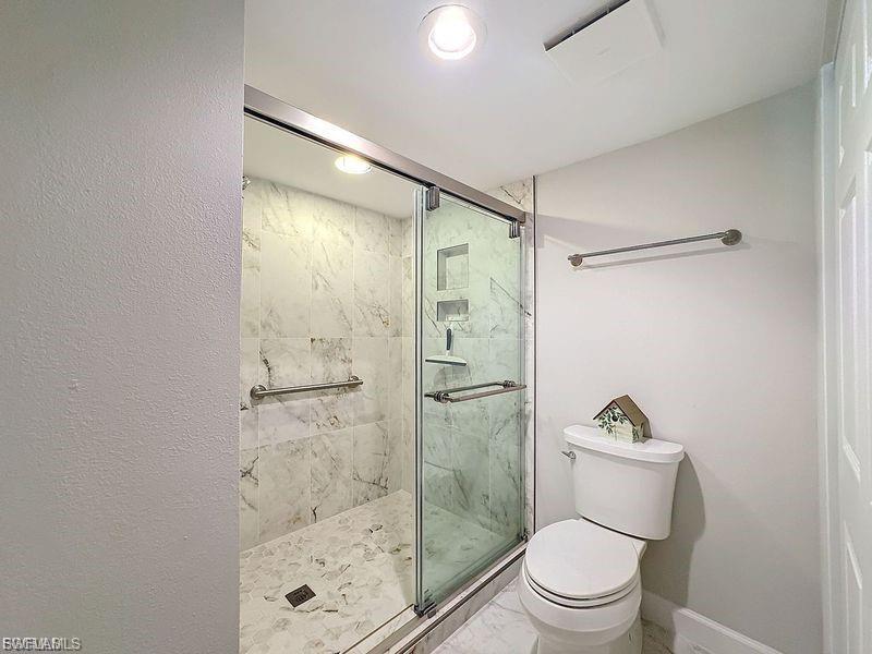 Full bath featuring a marble finish shower and marble look tiles