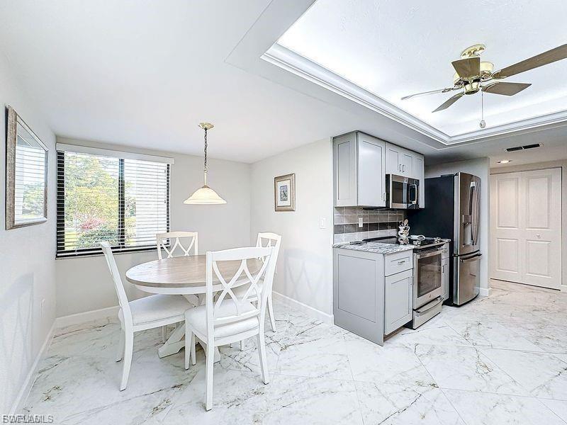 Kitchen with gray cabinetry, appliances with stainless steel finishes, light marble finish flooring, and decorative backsplash