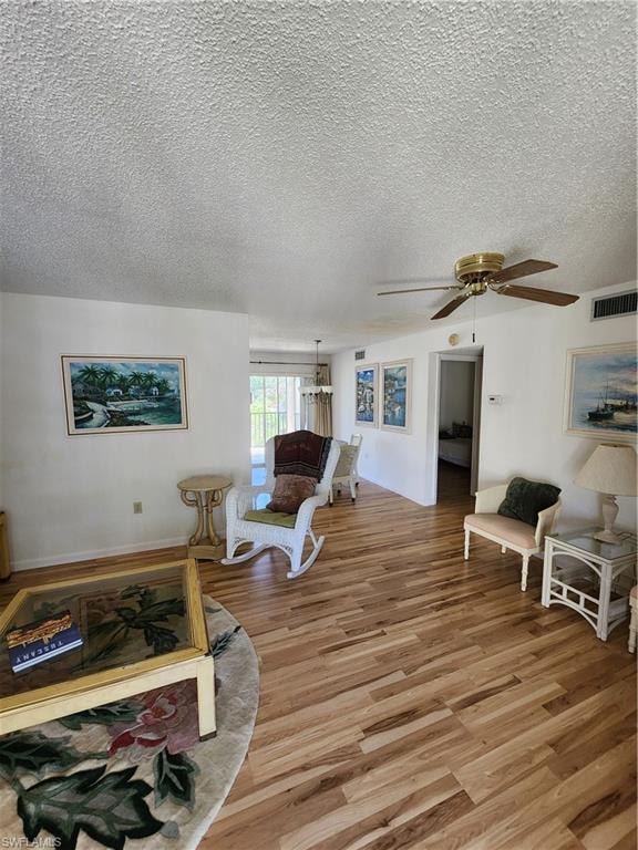 Living area featuring light wood-style flooring, a textured ceiling, a ceiling fan, and a chandelier