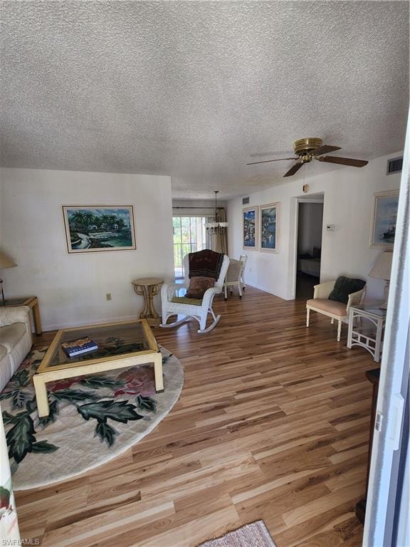 Living room with light wood finished floors, ceiling fan, a textured ceiling, and a chandelier
