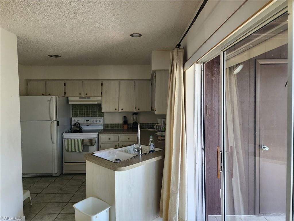 Kitchen featuring white appliances, light tile patterned floors, a textured ceiling, under cabinet range hood, and light countertops
