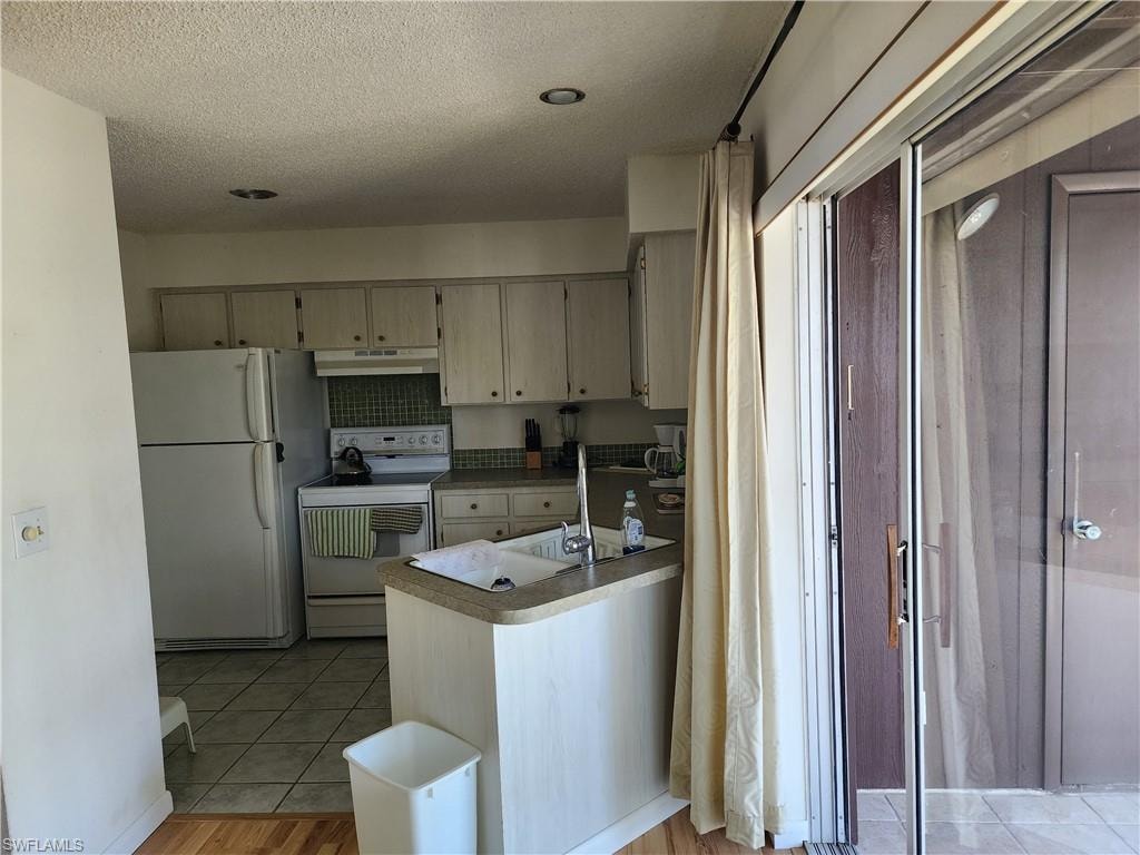 Kitchen featuring white appliances, a textured ceiling, light countertops, under cabinet range hood, and light wood-style flooring