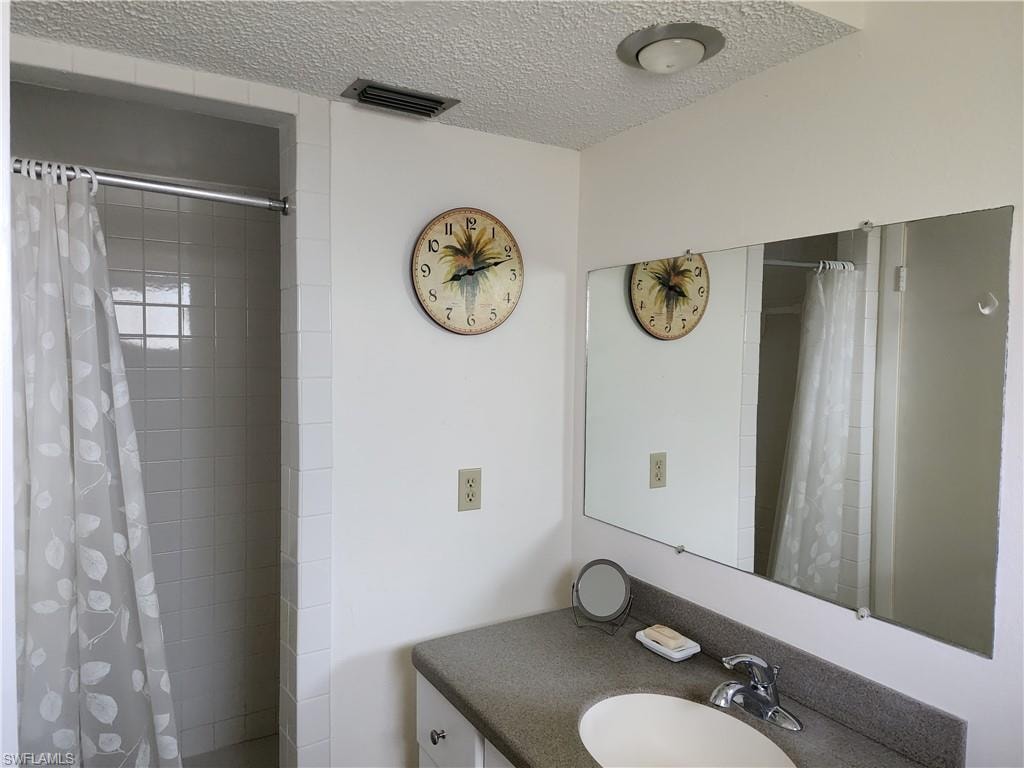 Full bathroom featuring vanity, a textured ceiling, and tiled shower