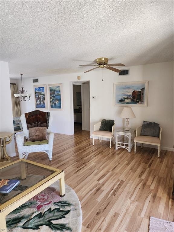 Living area featuring a textured ceiling, light wood finished floors, a chandelier, and ceiling fan