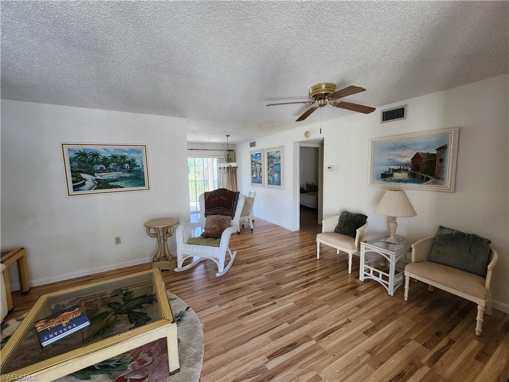 Living area with wood finished floors, a textured ceiling, a ceiling fan, and a chandelier