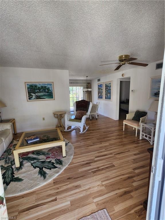 Living area with light wood finished floors, ceiling fan, and a textured ceiling