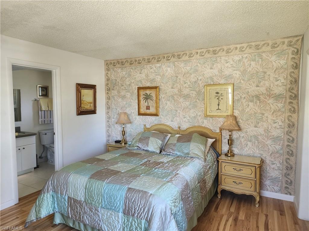 Bedroom with a textured ceiling, wood finished floors, wallpapered walls, and connected bathroom