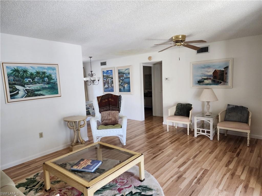 Living area with a textured ceiling, a chandelier, light wood finished floors, and a ceiling fan