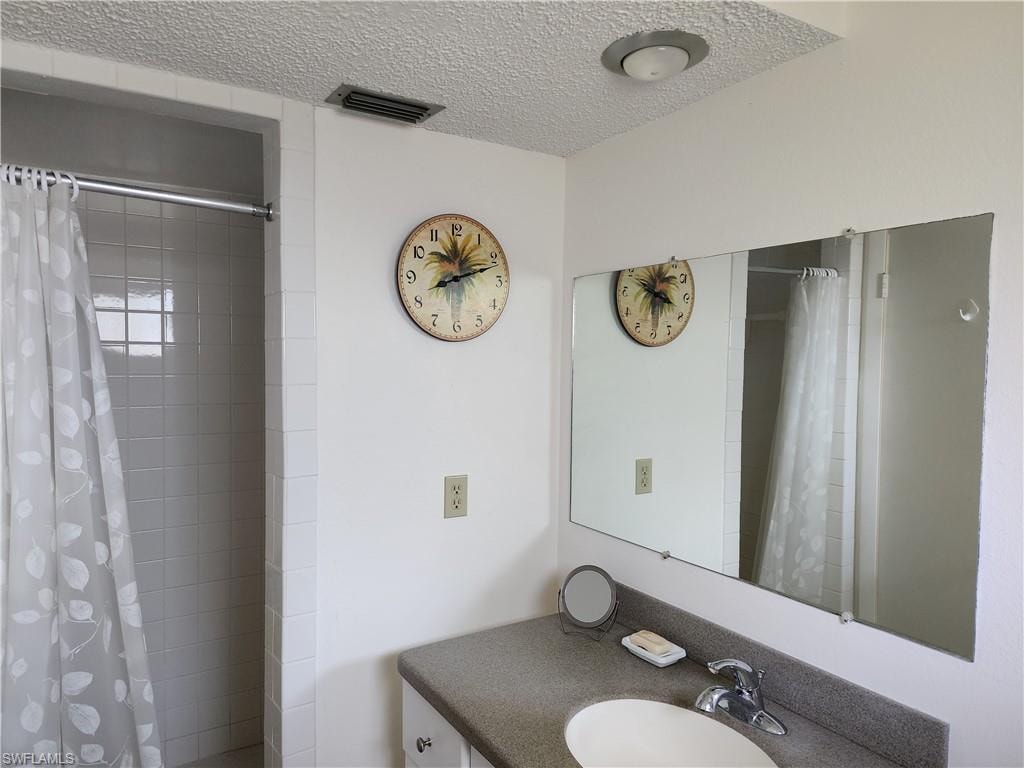 Full bath with vanity, tiled shower, and a textured ceiling