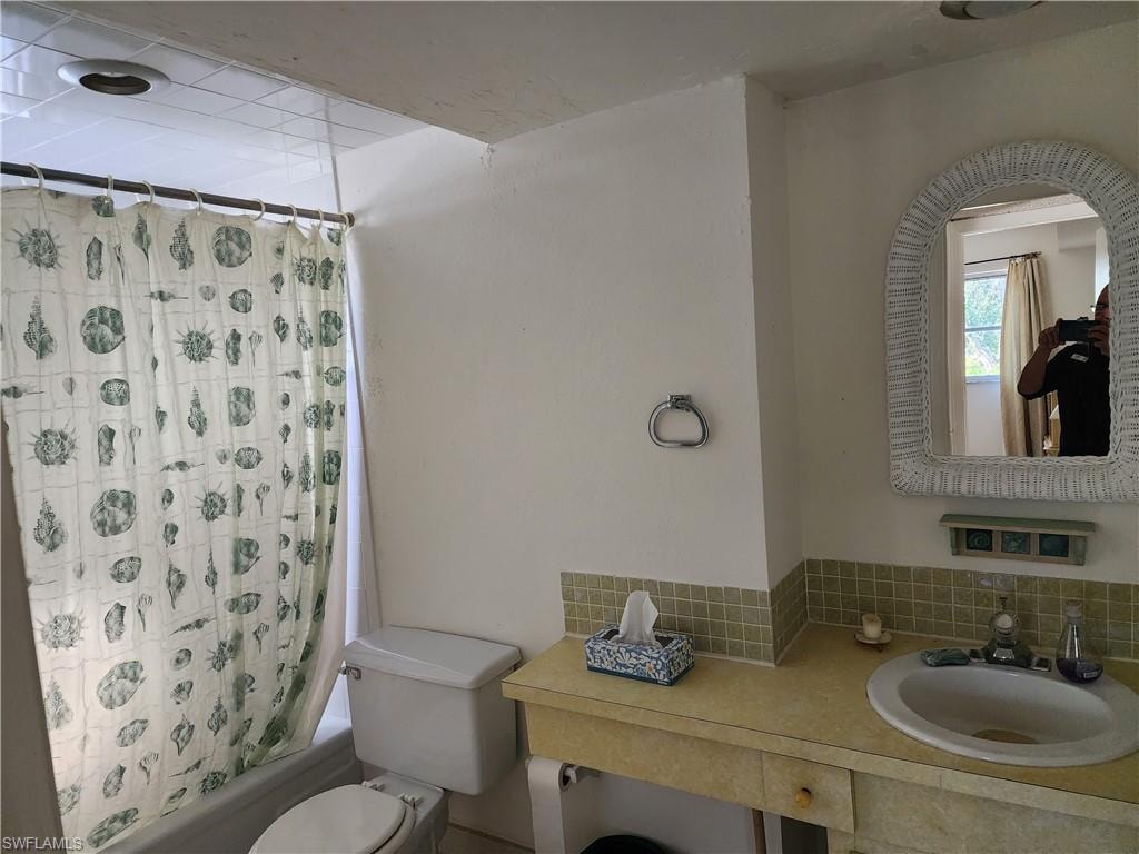 Full bath featuring shower / tub combo, vanity, and decorative backsplash