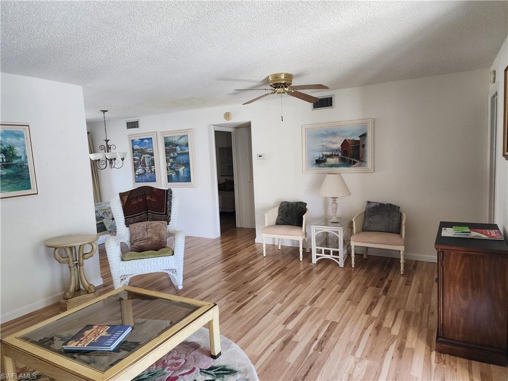 Living area with a textured ceiling, light wood-type flooring, a ceiling fan, and a chandelier