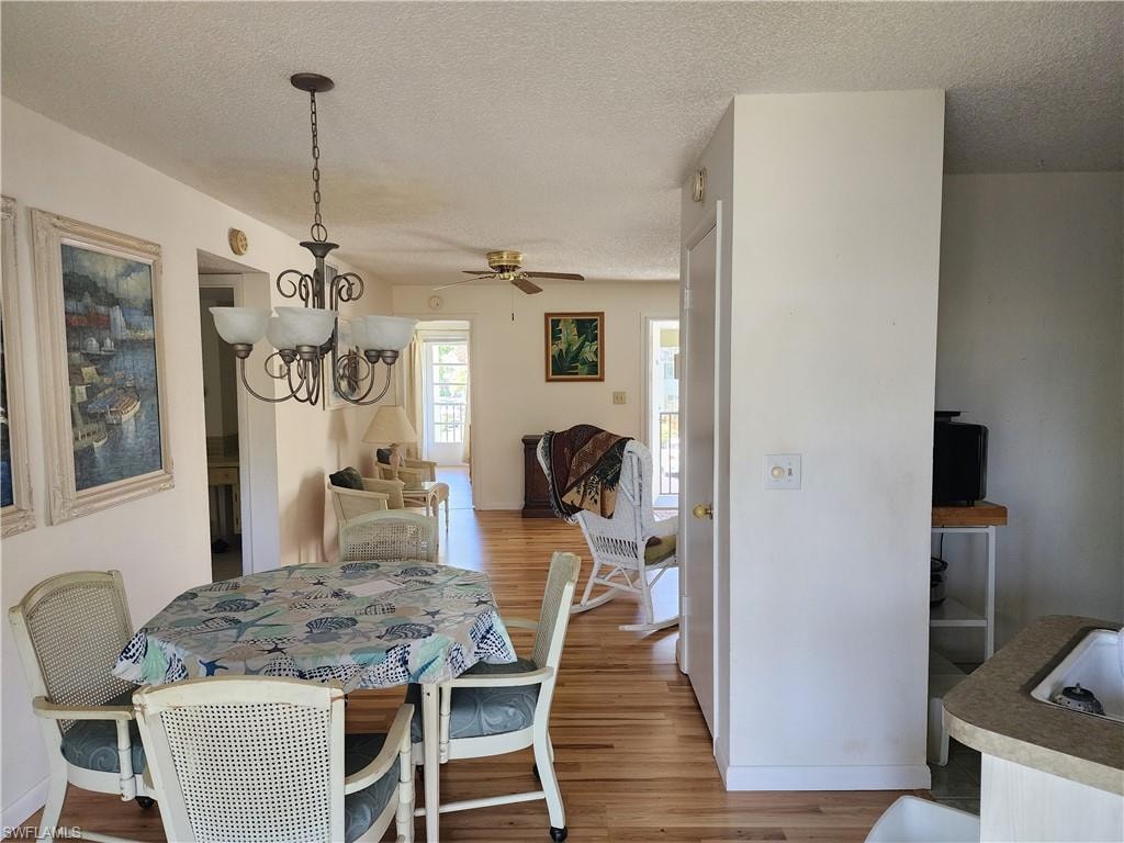 Dining space featuring light wood finished floors, a textured ceiling, a chandelier, and ceiling fan
