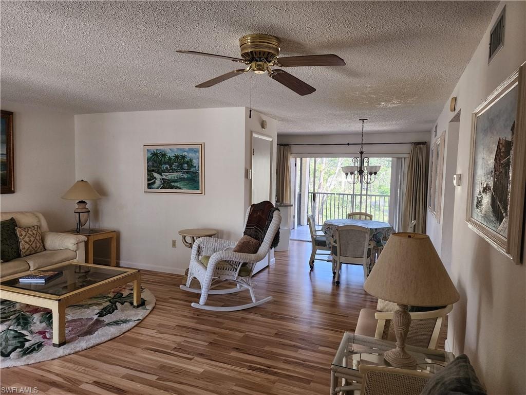 Living room with wood finished floors, a chandelier, a textured ceiling, and ceiling fan