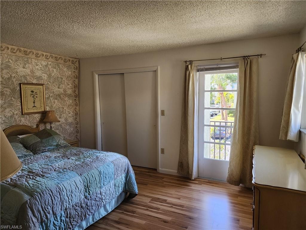 Bedroom with a textured ceiling, wood finished floors, wallpapered walls, a closet, and an accent wall