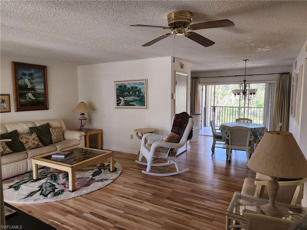 Living room with a chandelier, a ceiling fan, wood finished floors, and a textured ceiling