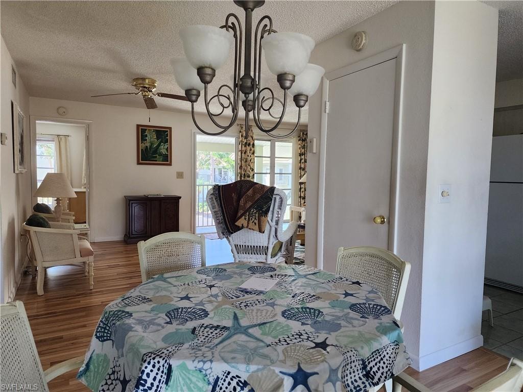 Dining area featuring a chandelier, a textured ceiling, healthy amount of natural light, wood finished floors, and a ceiling fan