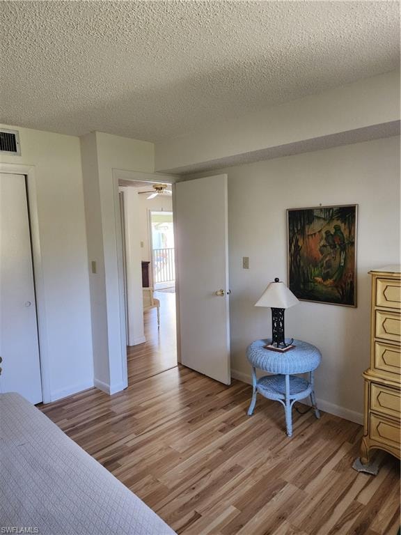 Bedroom with light wood finished floors, a textured ceiling, and a closet