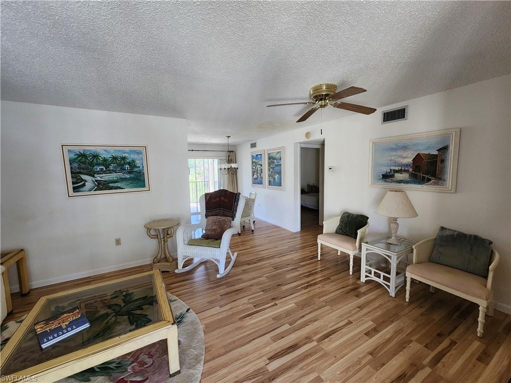 Living area featuring wood finished floors, a textured ceiling, a ceiling fan, and a chandelier