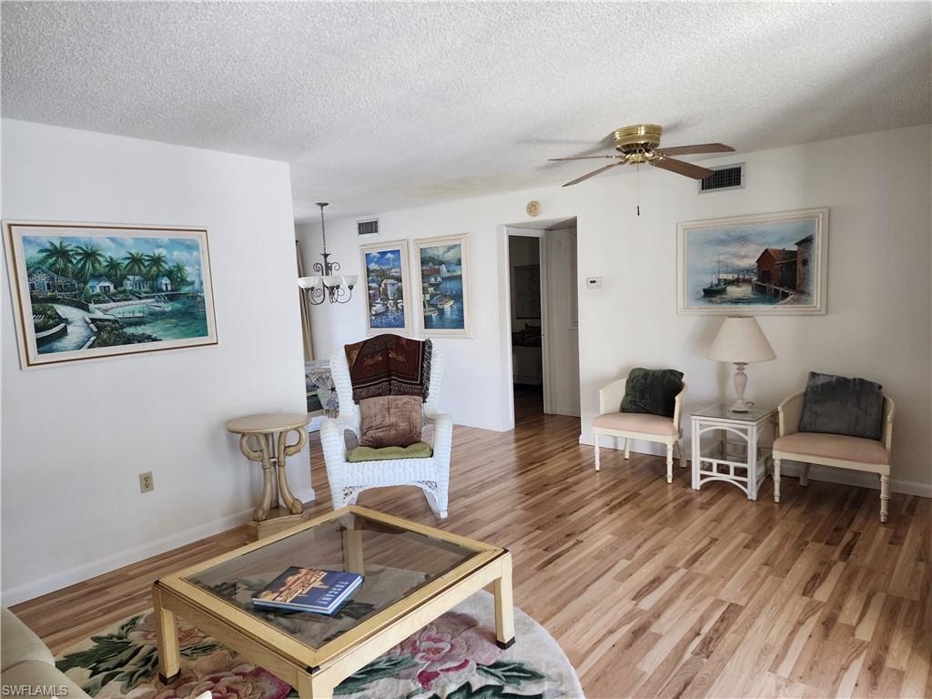 Living area featuring a textured ceiling, a chandelier, light wood-type flooring, and a ceiling fan