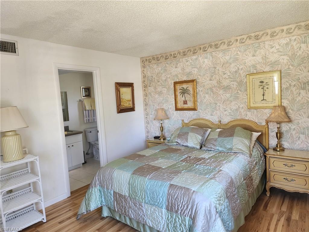 Bedroom with a textured ceiling, wood finished floors, and ensuite bath