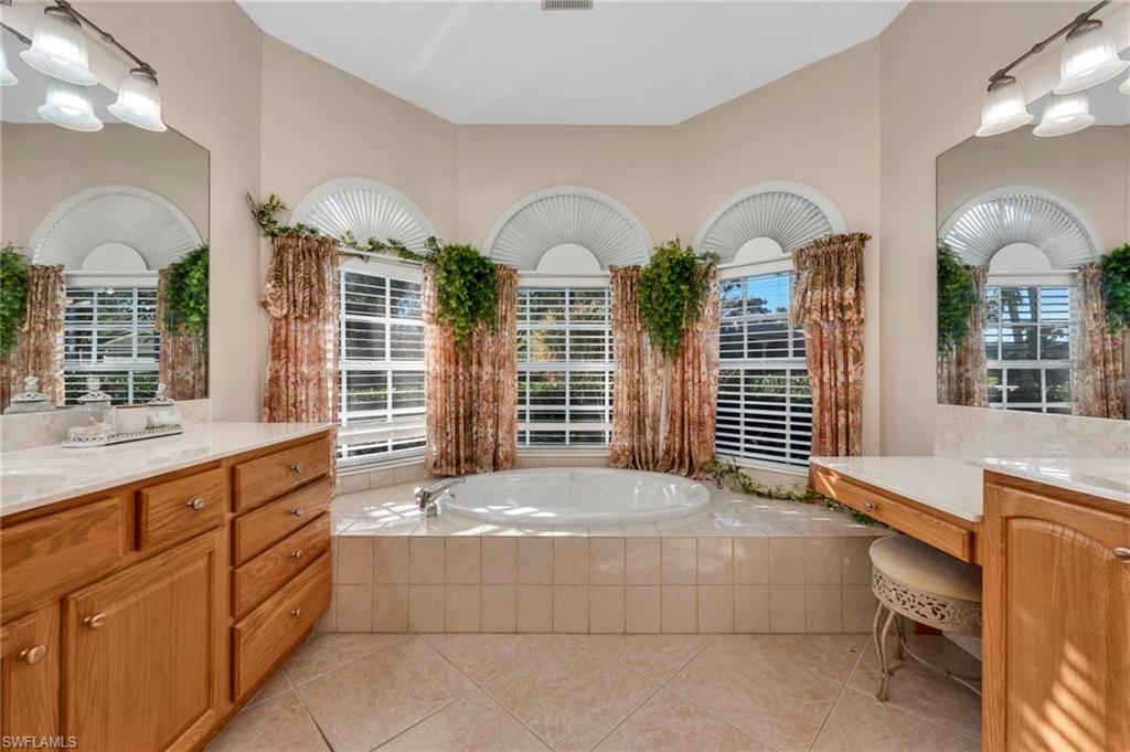 Primary bath featuring a garden tub, two vanities, and light tile patterned floors