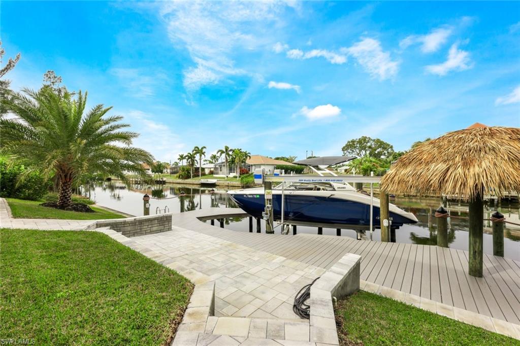 Dock area with boat lift, a water view, and a lawn