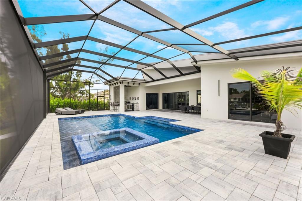 View of swimming pool featuring a sunroom, a patio area, a pool with connected hot tub, and glass enclosure