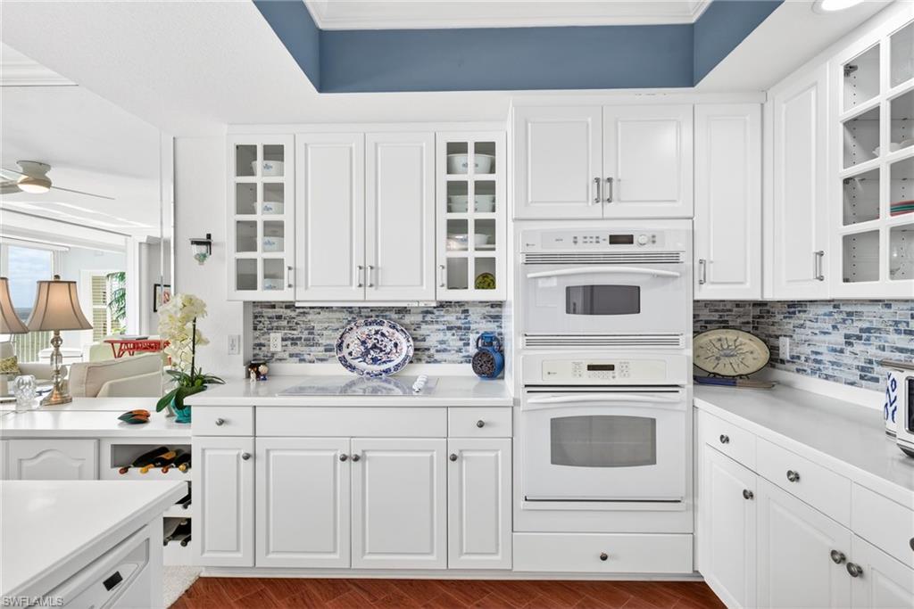 Kitchen featuring glass insert cabinets, white cabinets, white double oven, crown molding, and a raised ceiling