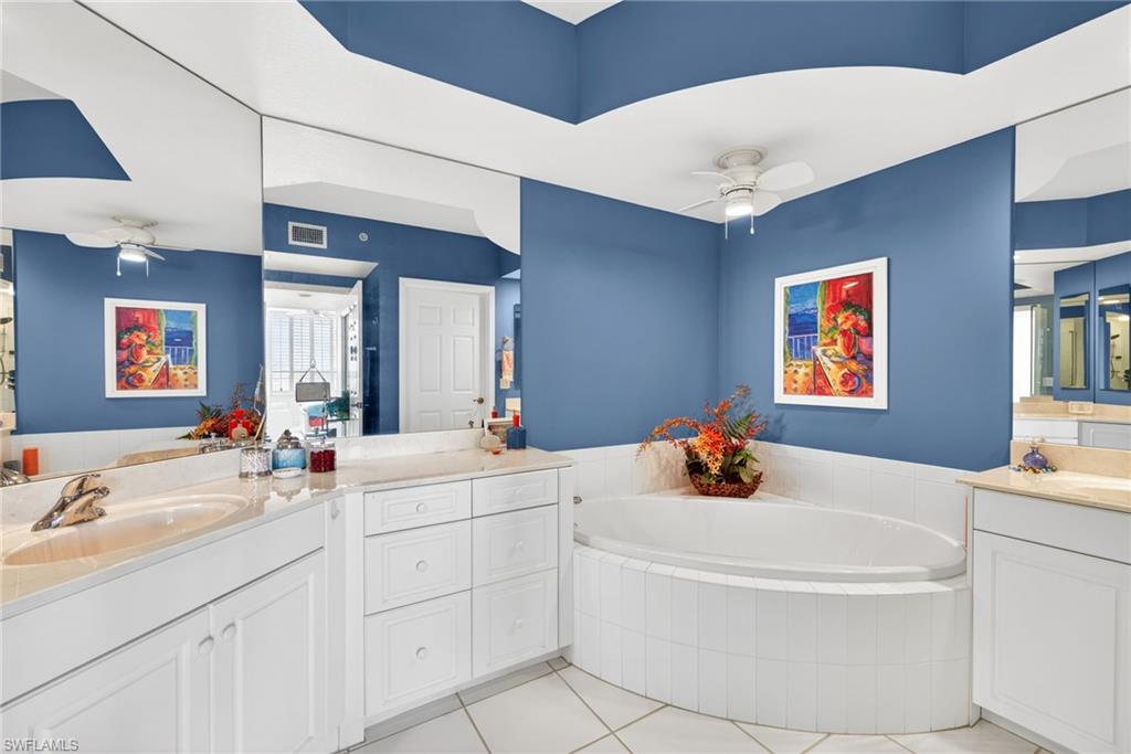 Bathroom featuring a ceiling fan, a garden tub, two vanities, and light tile patterned floors